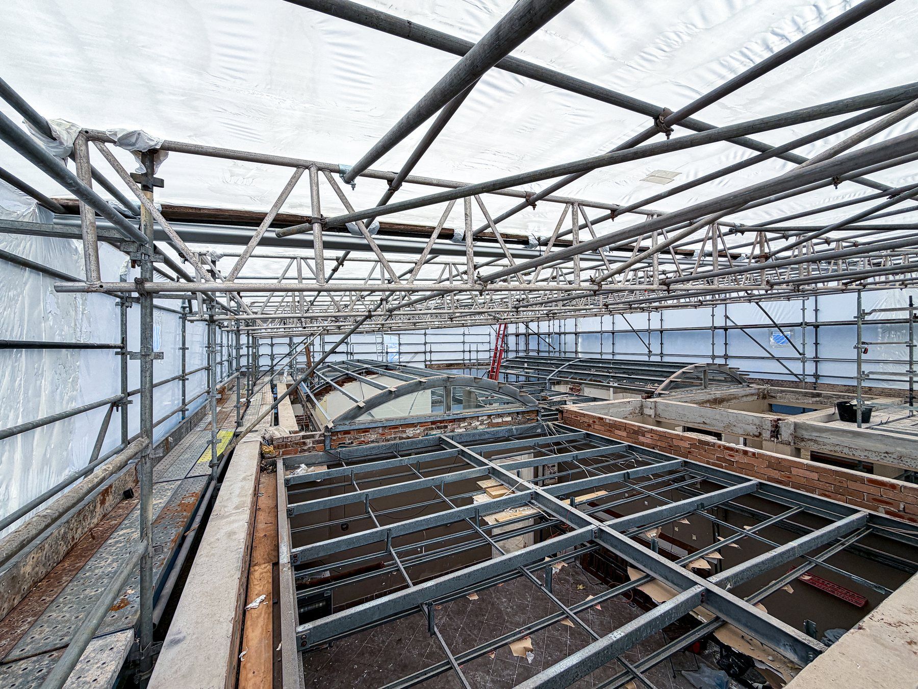 Inside the wrap: scaffold beams and the white shrink wrap roof over the house stripped back to its frame