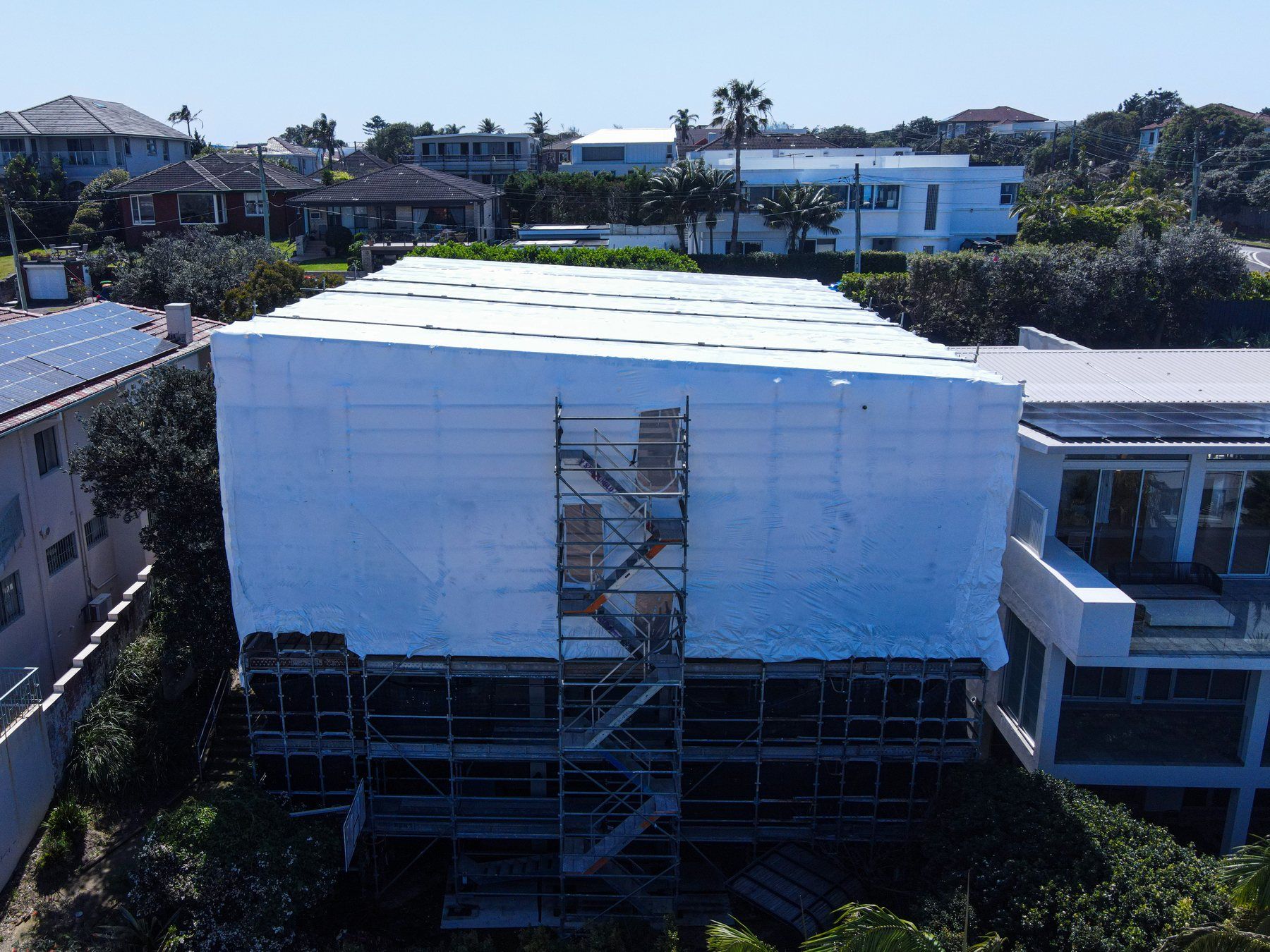 Front of the wrapped home from the air, the scaffold stair tower running up the face