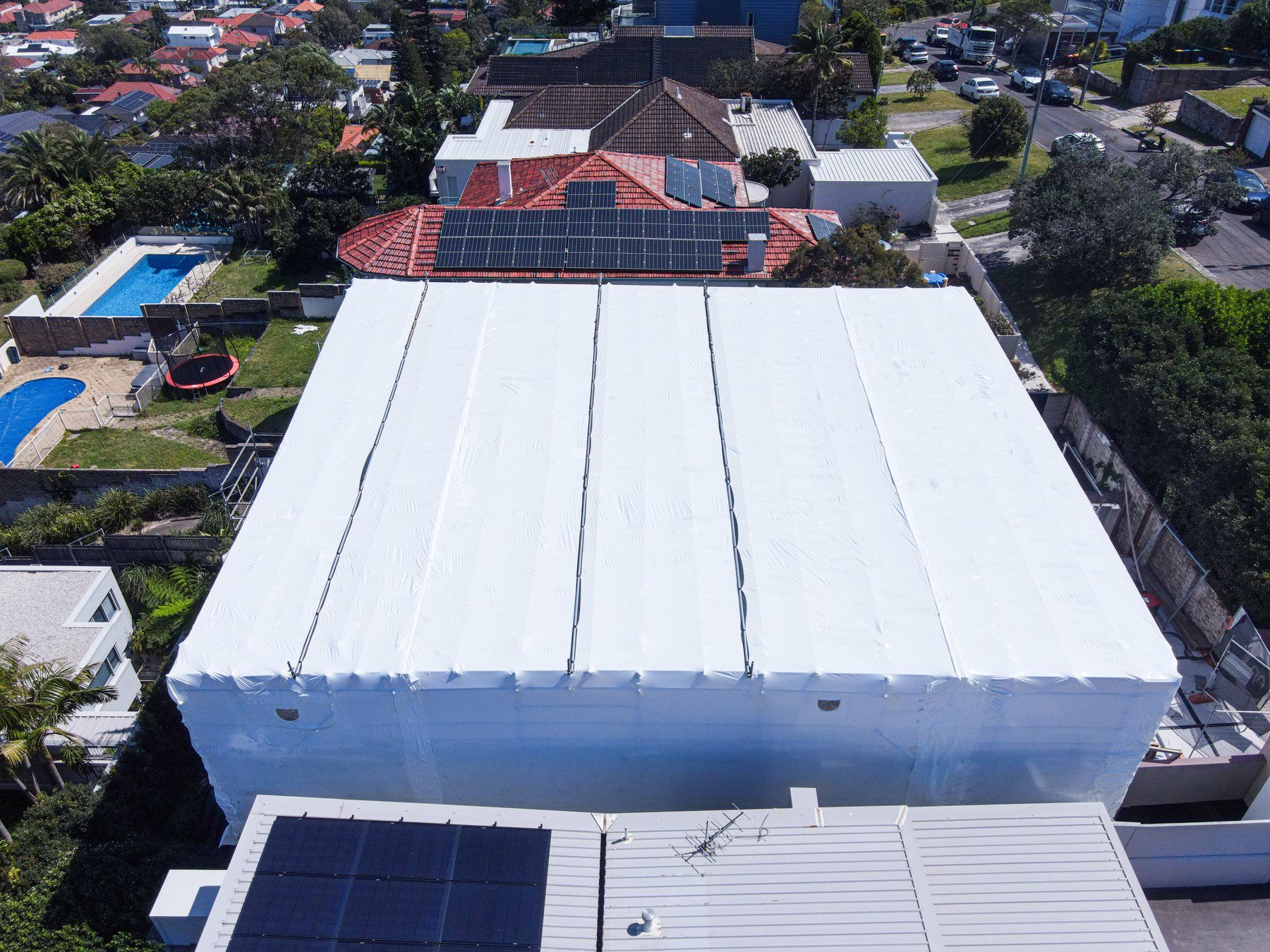 Closer aerial of the shrink wrap roof, pools and gardens in the backyards behind