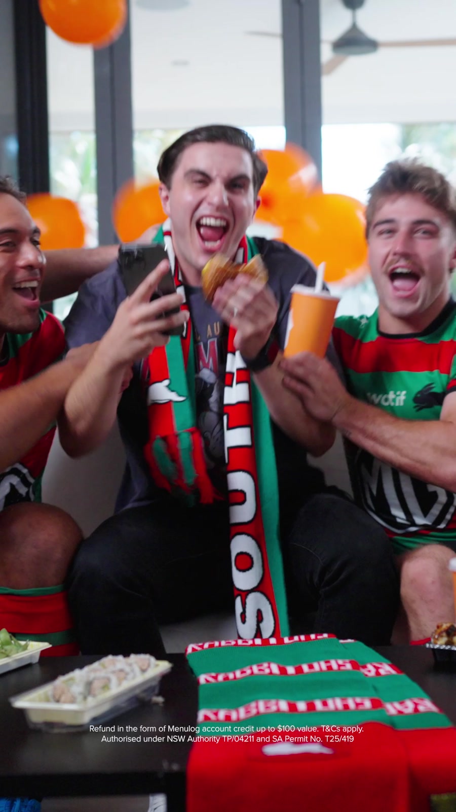 9:16 frame of the same moment: tight on the fan with the burger, phone and Menulog cup