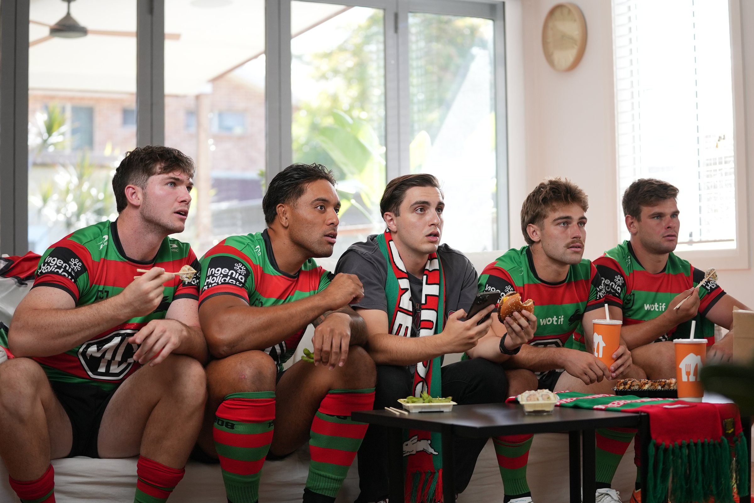 Five on the couch, the fan in the middle with his phone out, the players leaning in to watch